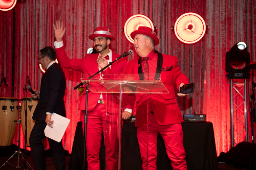 Two men in red suits and top hats at podium.